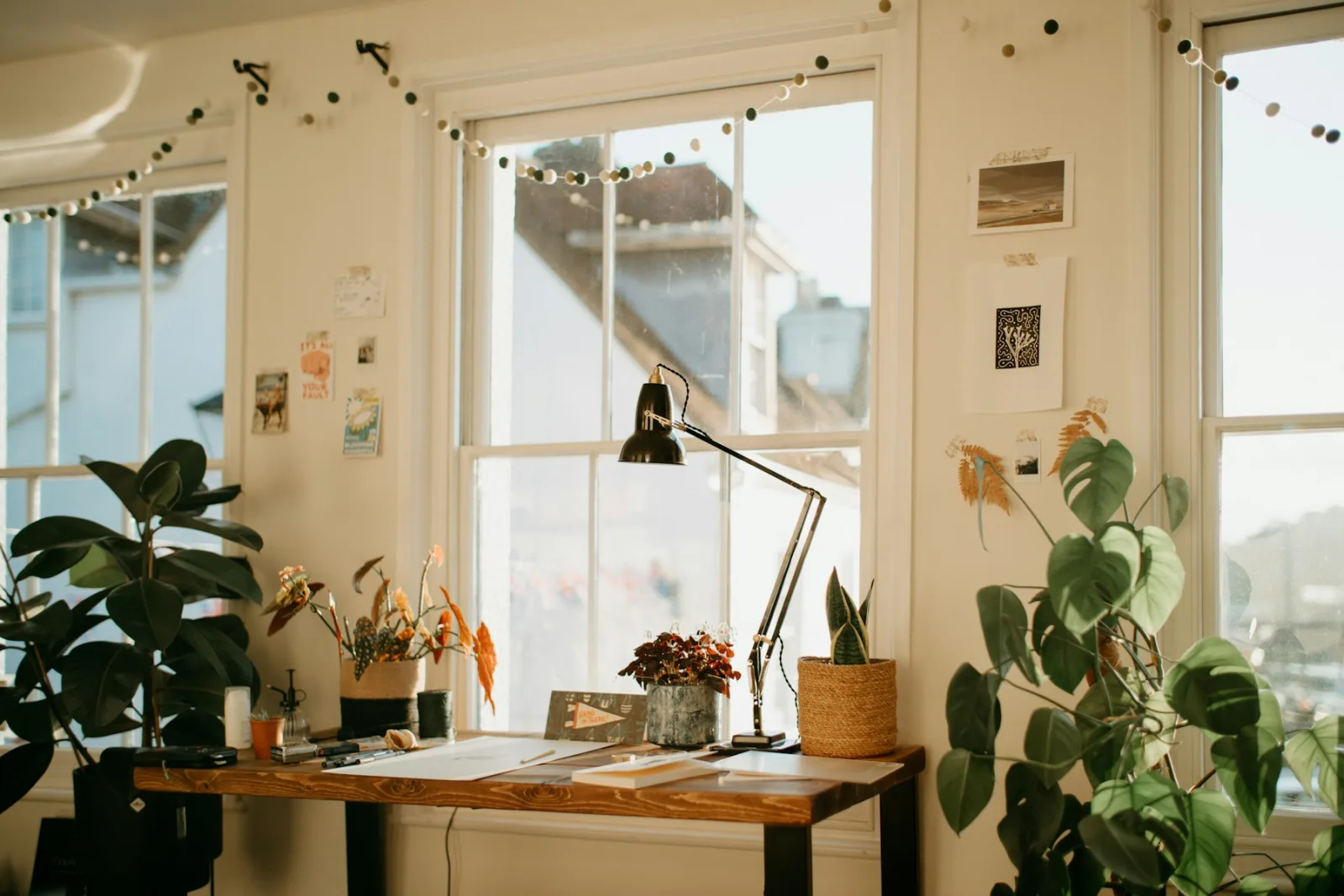 Bureau en bois devant une fenêtre lumineuse, avec une lampe d'architecte et des plantes