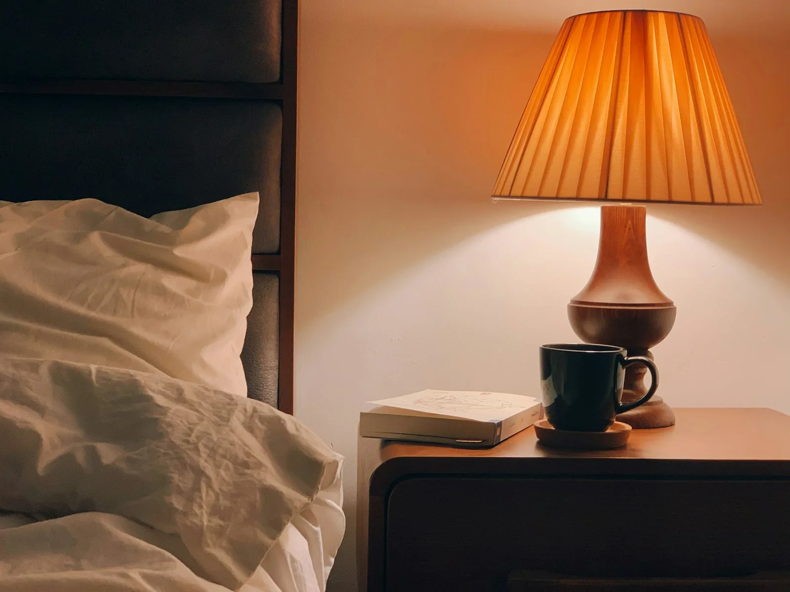Lampe de chevet allumée à abat-jour plissé sur une table de nuit, à côté du lit