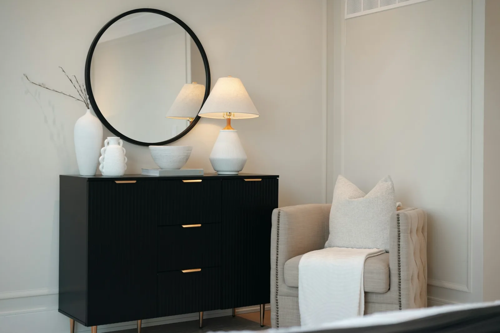 Miroir rond au-dessus d'une commode noire avec une lampe à poser