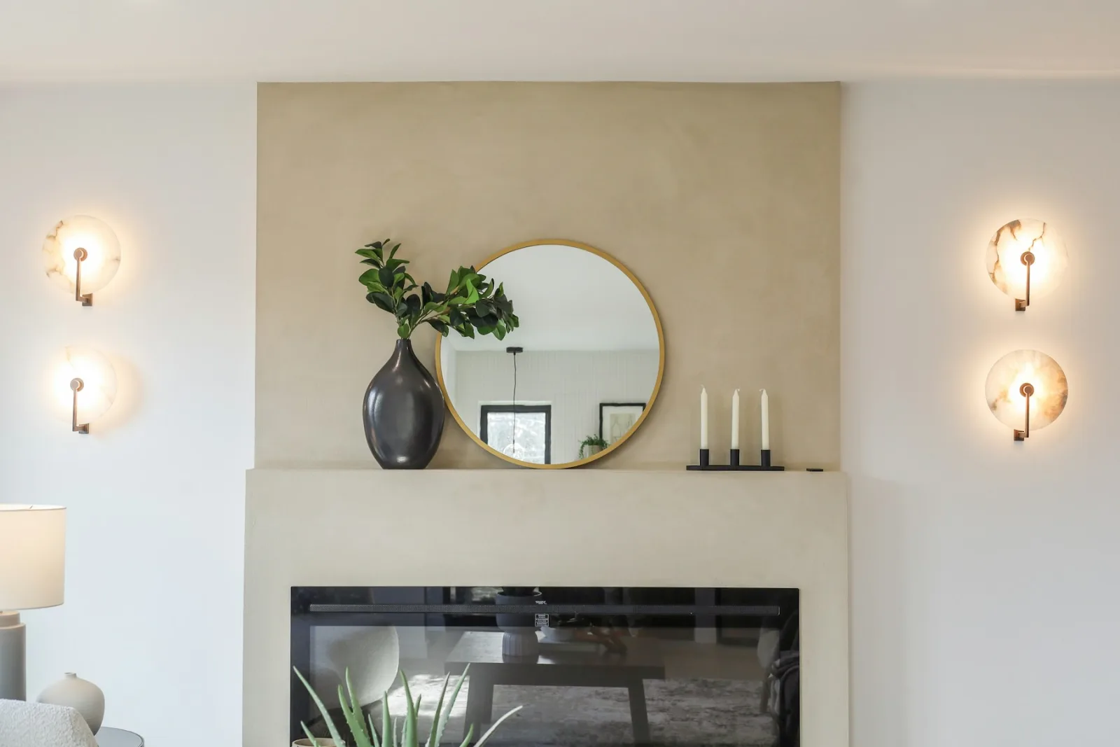 Miroir rond au-dessus d'une cheminée blanche entre deux appliques