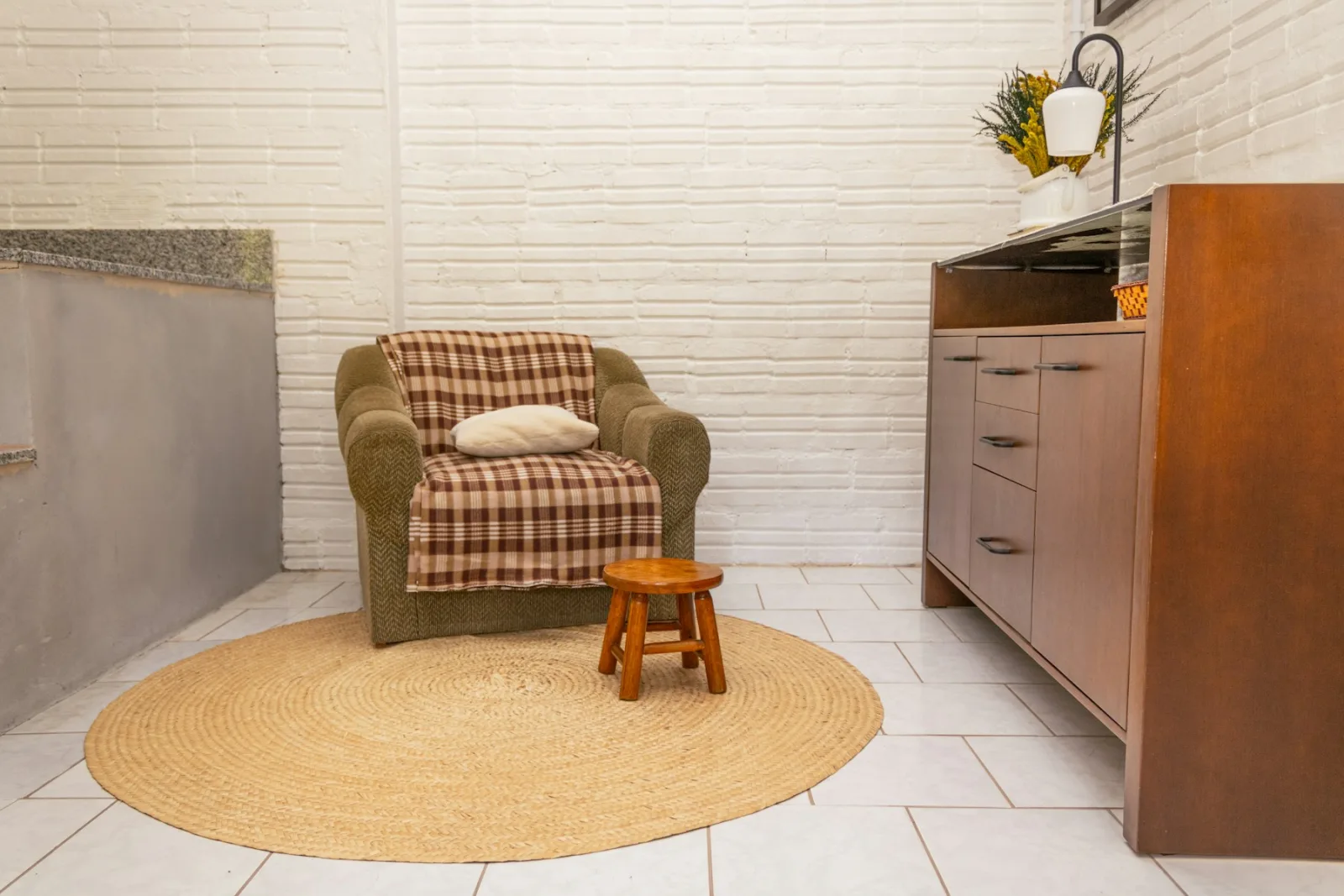 Tapis rond en jute sous un fauteuil à carreaux et un petit tabouret en bois
