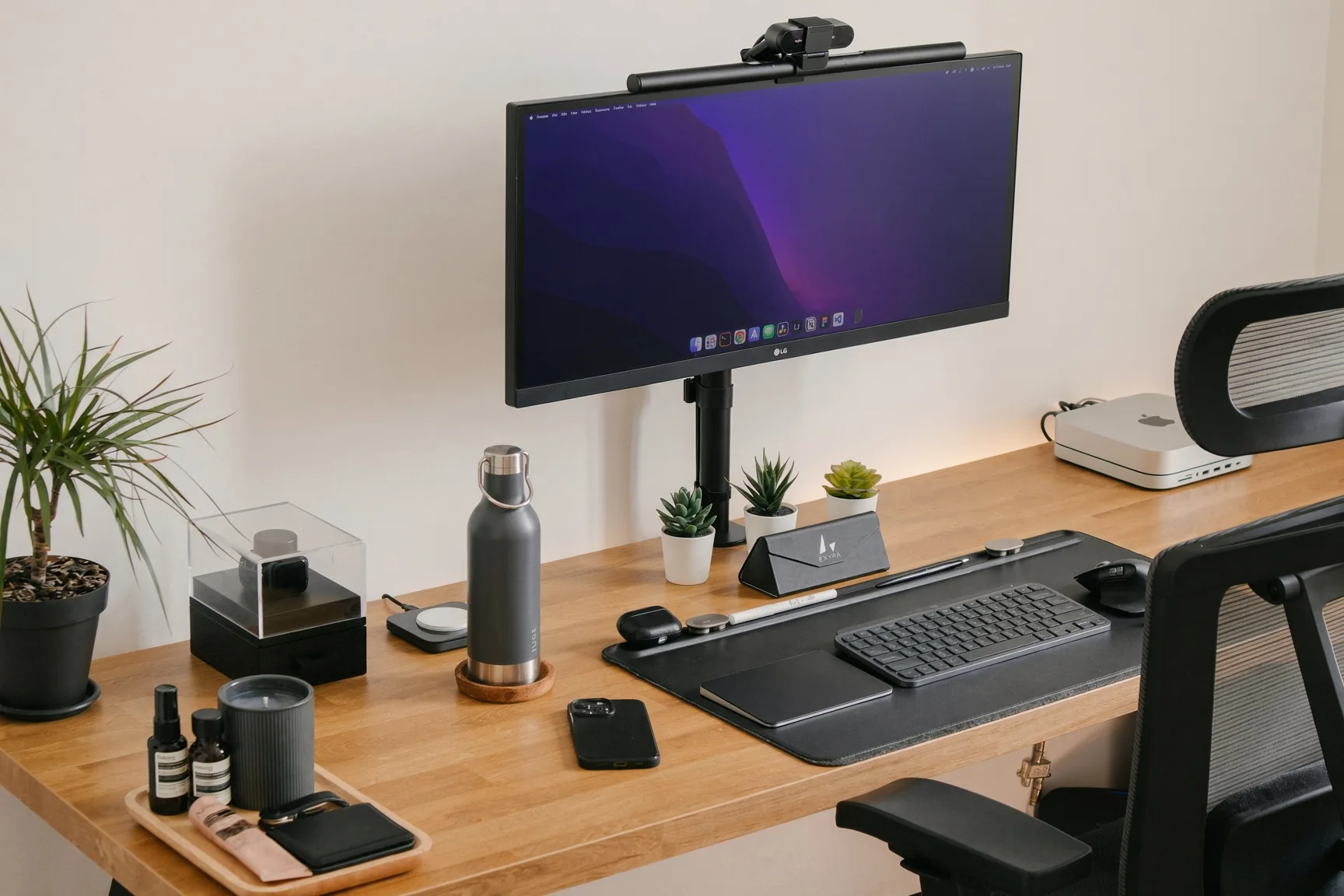 Bureau en bois avec un écran sur bras, une barre lumineuse et des plantes