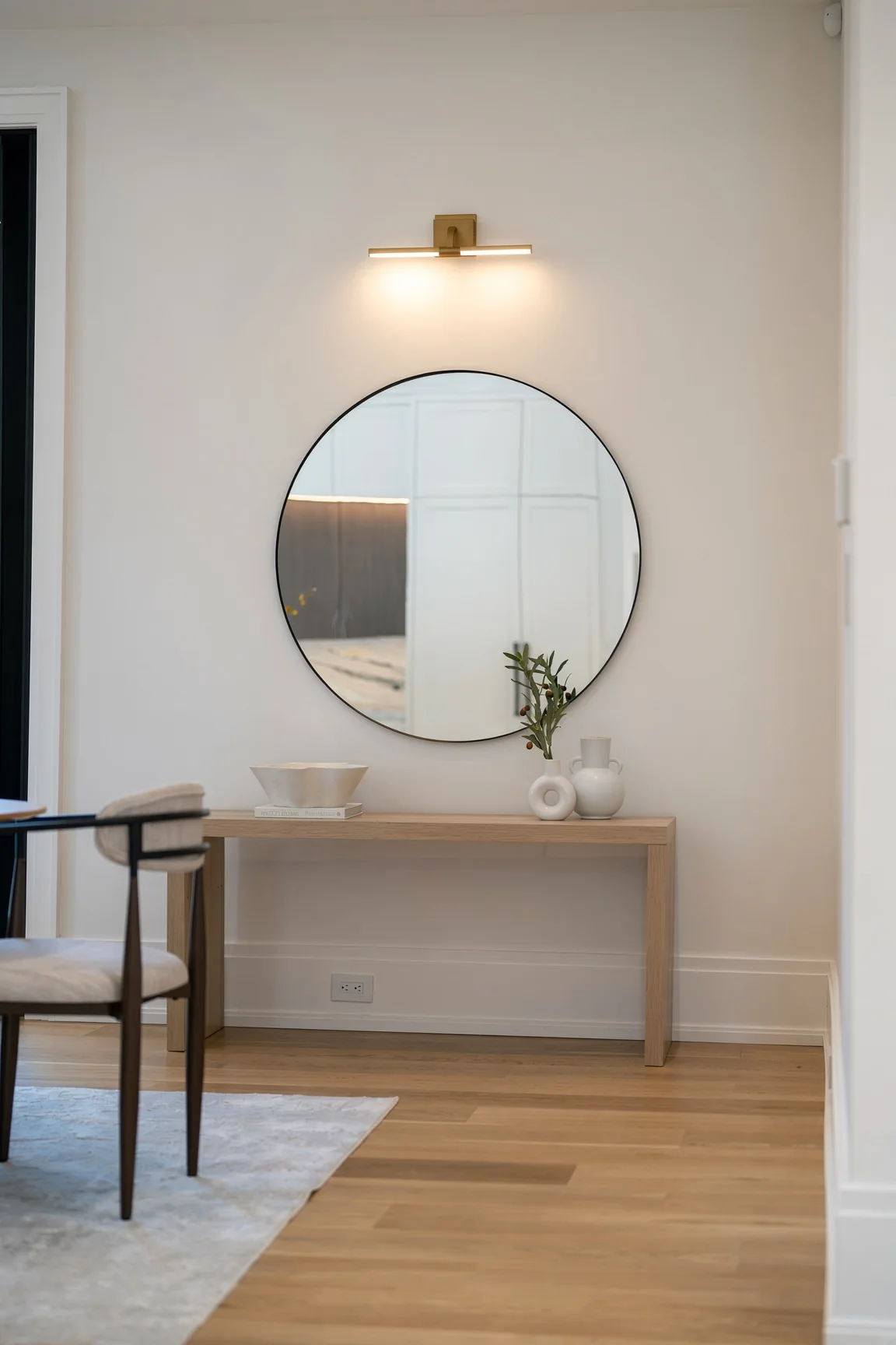 L'entrée : miroir rond au-dessus d'une console en bois clair, applique allumée
