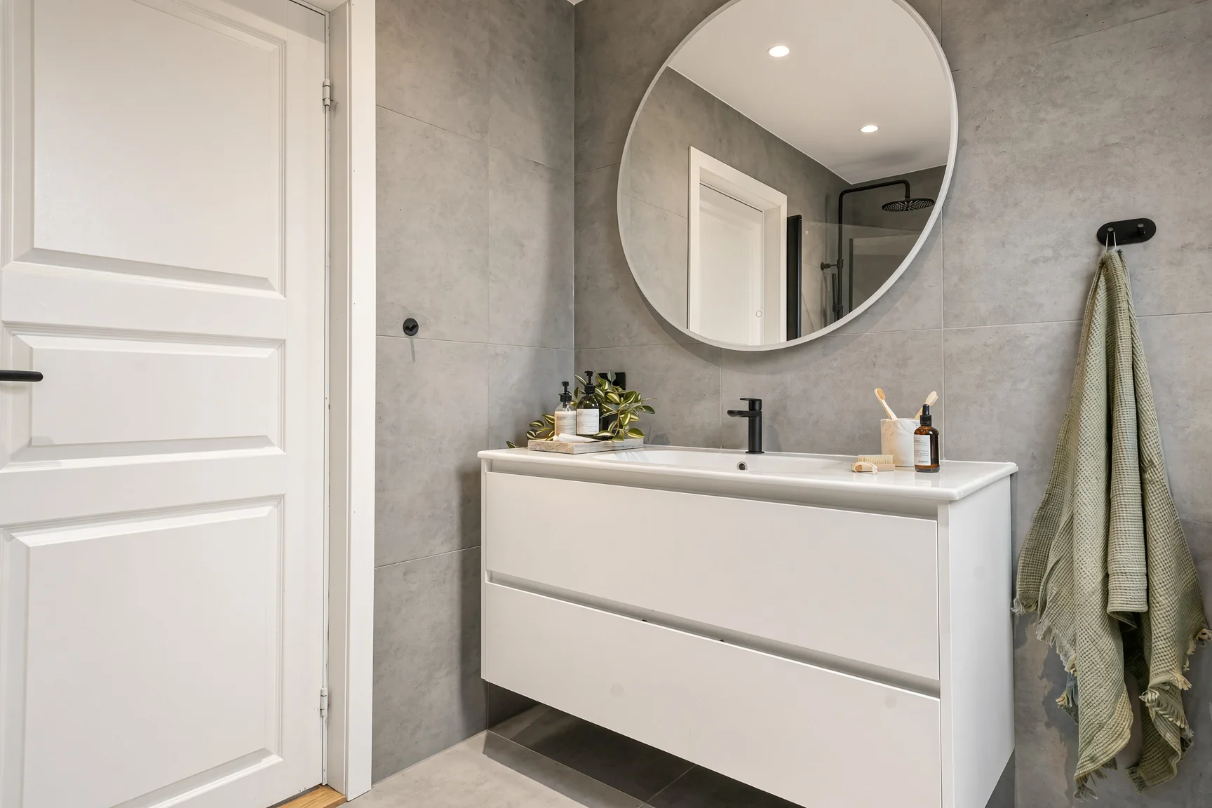La salle de bain : miroir rond et meuble vasque blanc sur mur gris